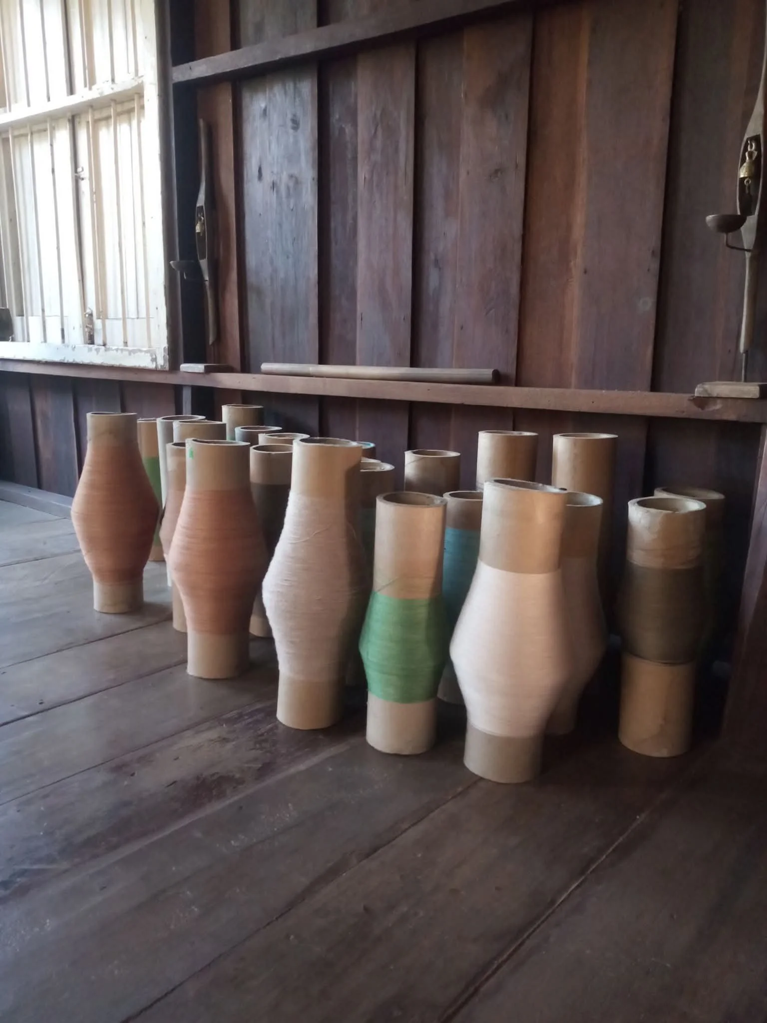 Une rangée de vases en terre cuite colorés, disposés sur un sol en bois dans un atelier ou un espace intérieur.