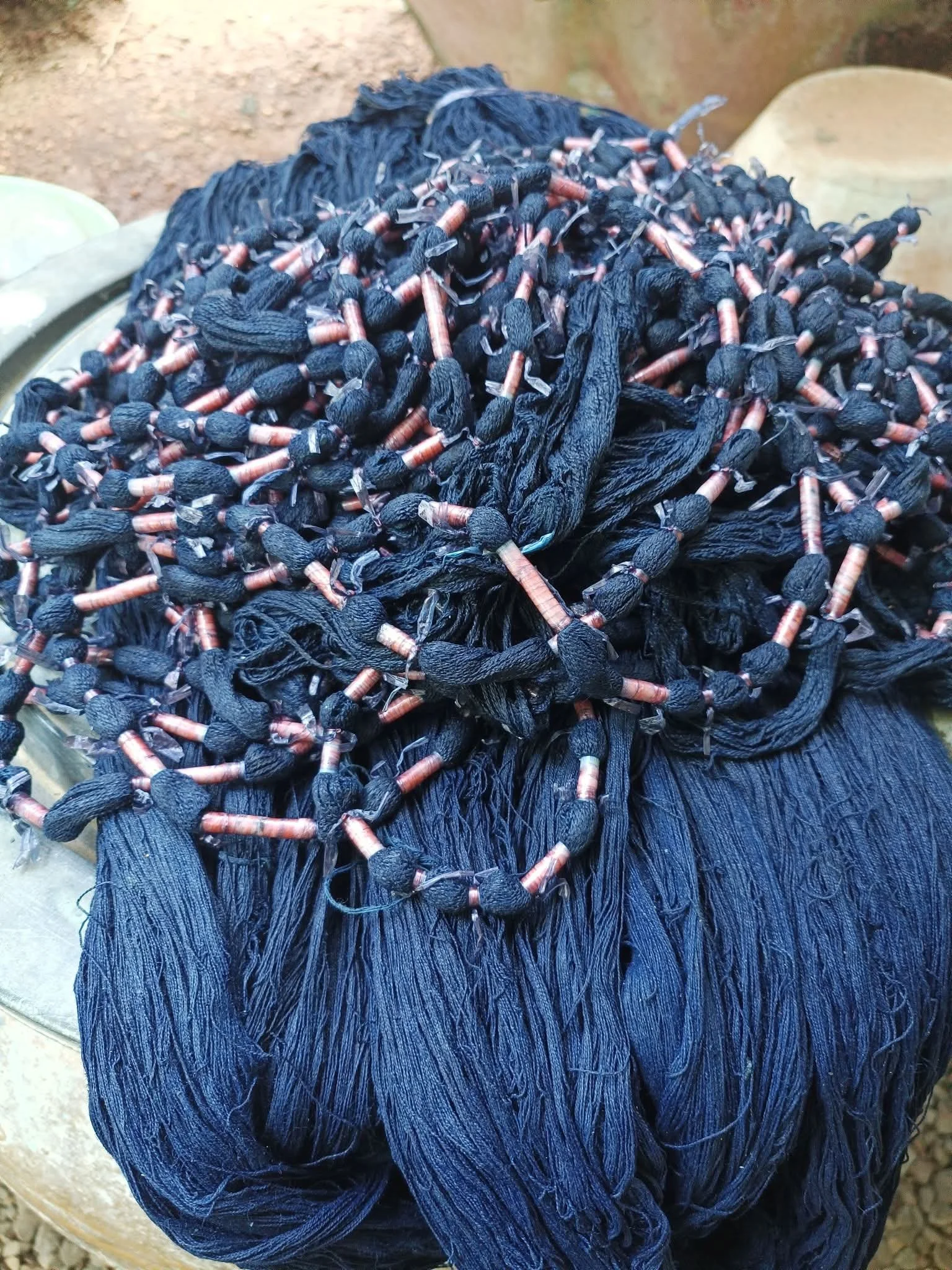 Un tas de fil noir avec des éléments métalliques colorés, semblant être des fils ou des tissus tissés, placé sur une surface. 
