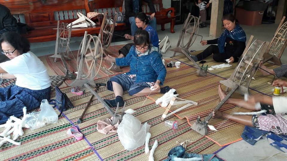 Groupe de personnes assises au sol en train de réparer des chaises, avec des outils et des matériaux.