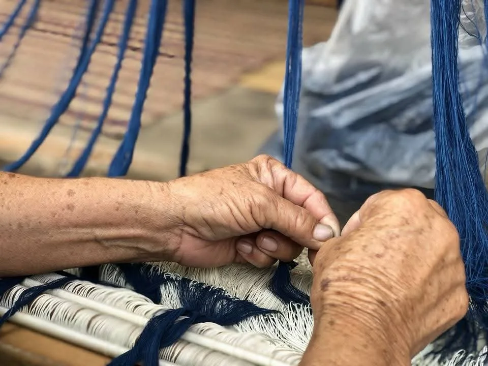 Mains de personne âgée tissant avec du fil bleu sur un métier à tisser.