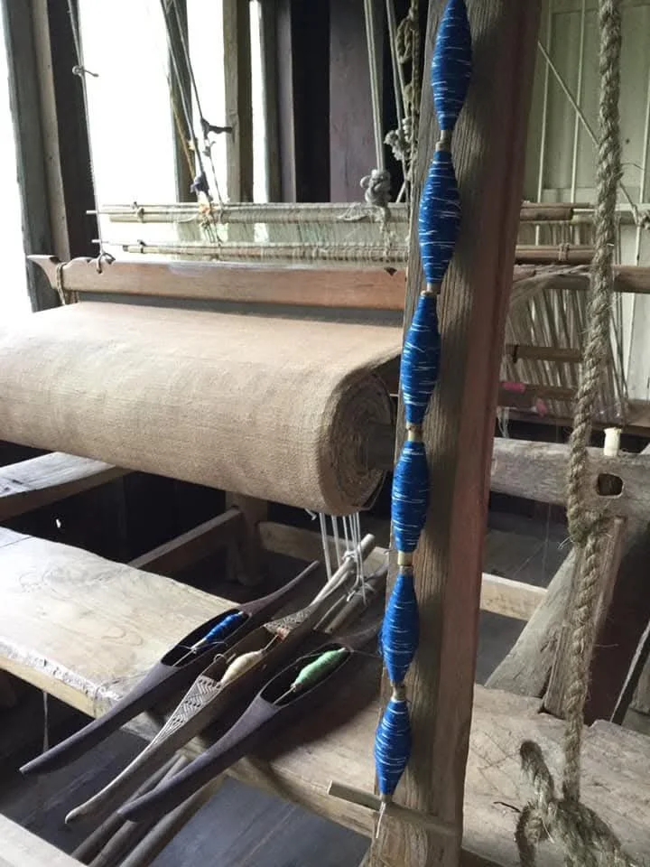 Une vieille machine à tisser en bois avec des éléments en corde et en tissu, situés dans un atelier ou une pièce ancienne.