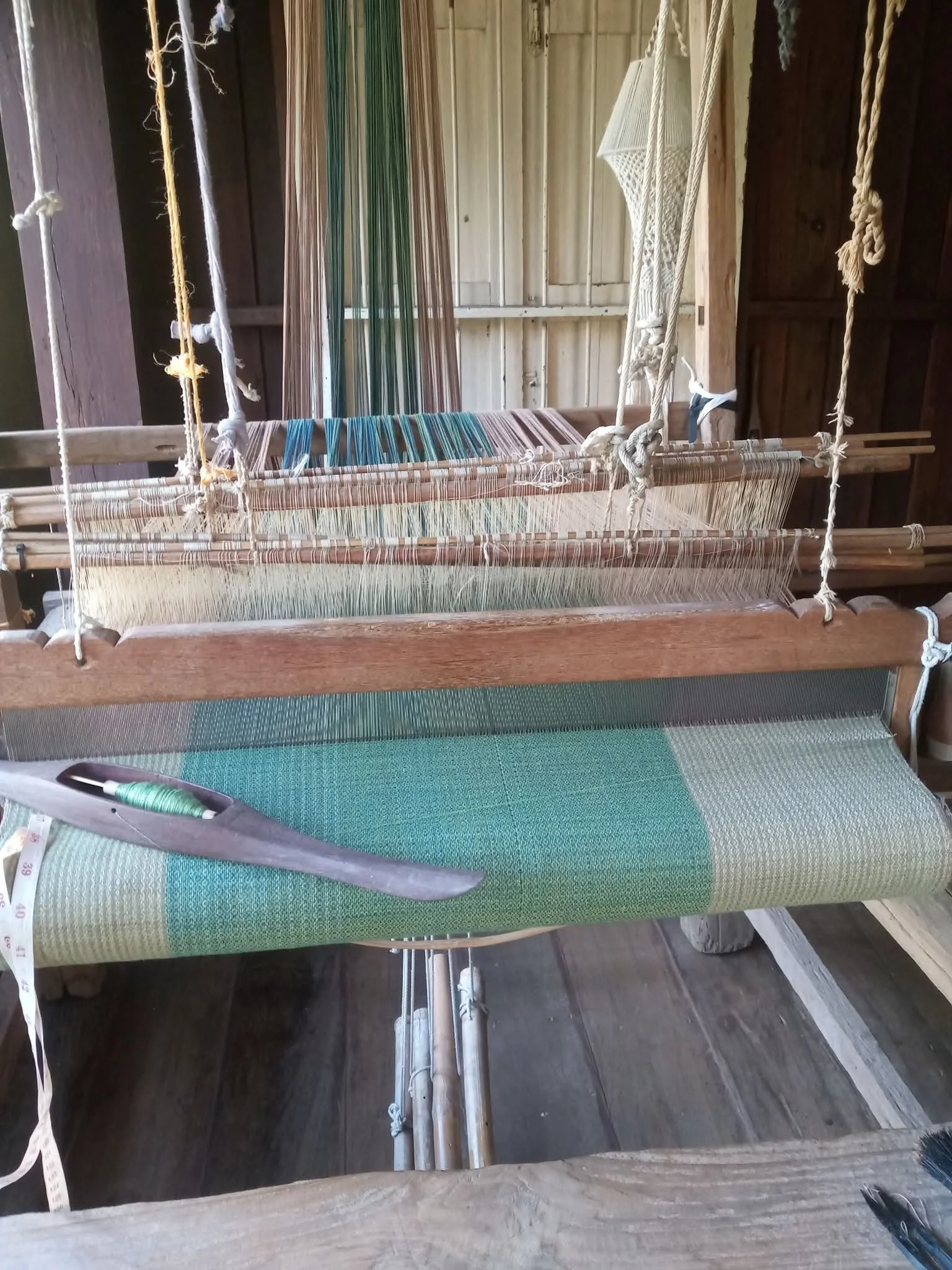 Un métier à tisser en bois avec du fil de canevas en place, situé dans une pièce en bois.