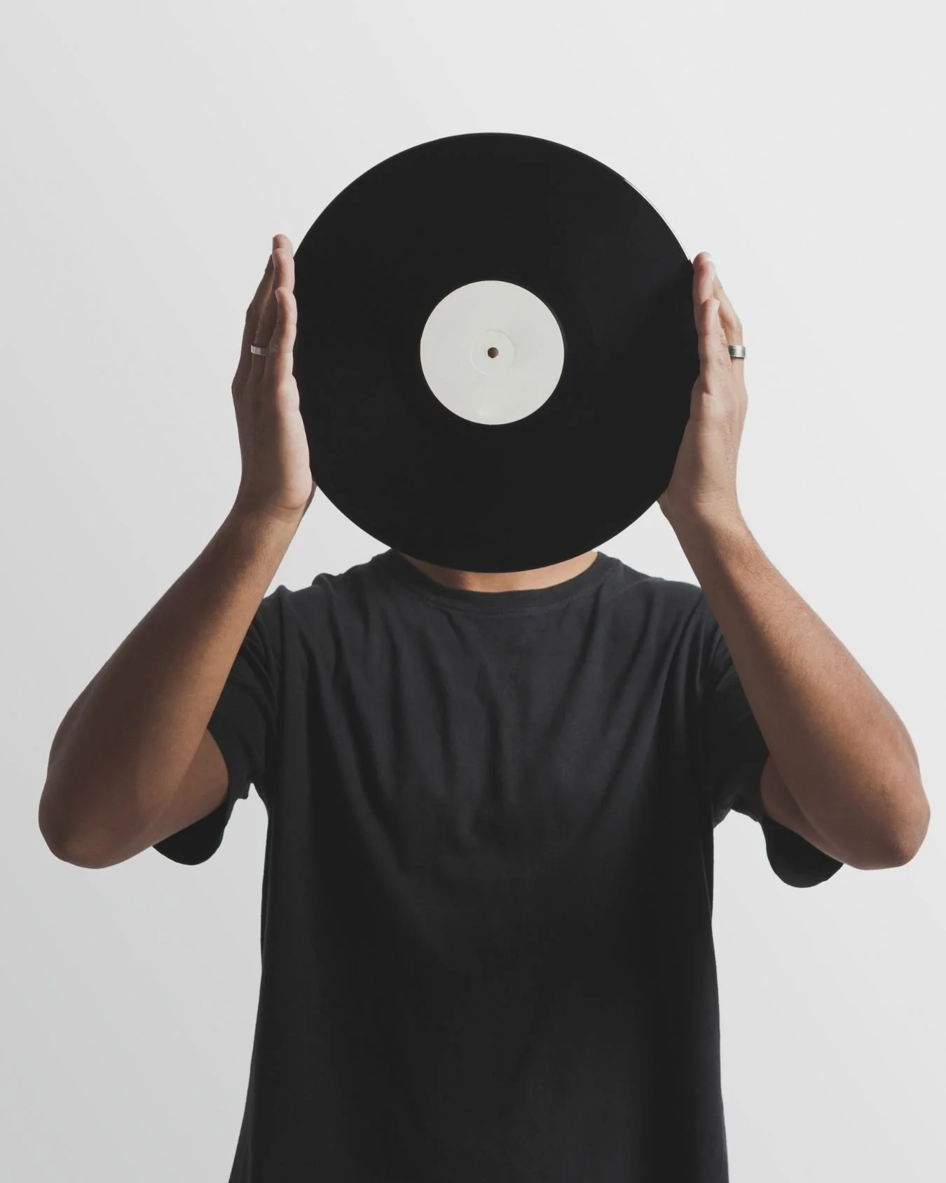 A man wearing a black t shirt and holding a vinyl record in front of his face.