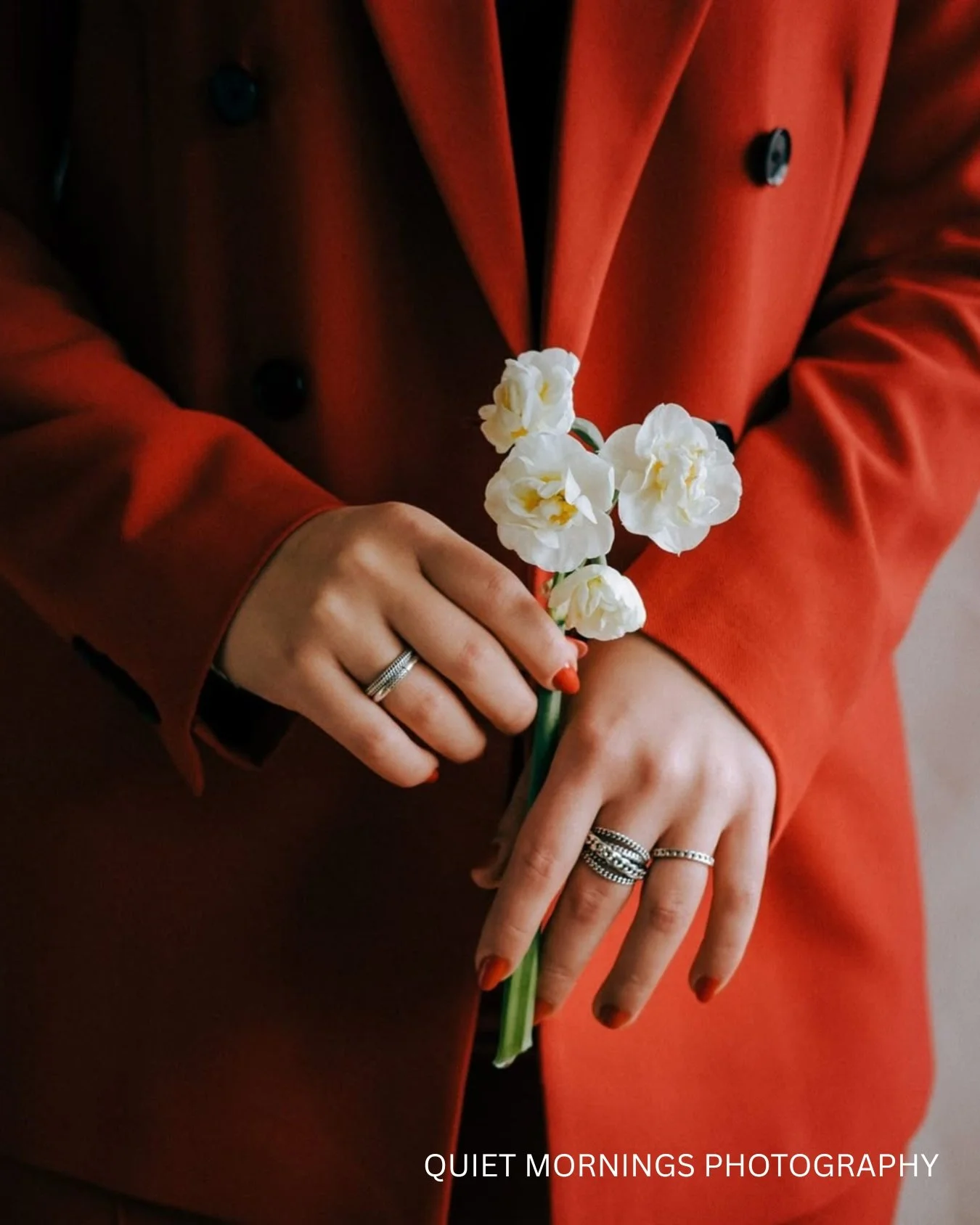 A close up of a bride wearing a red suit and holding some white flowers. 