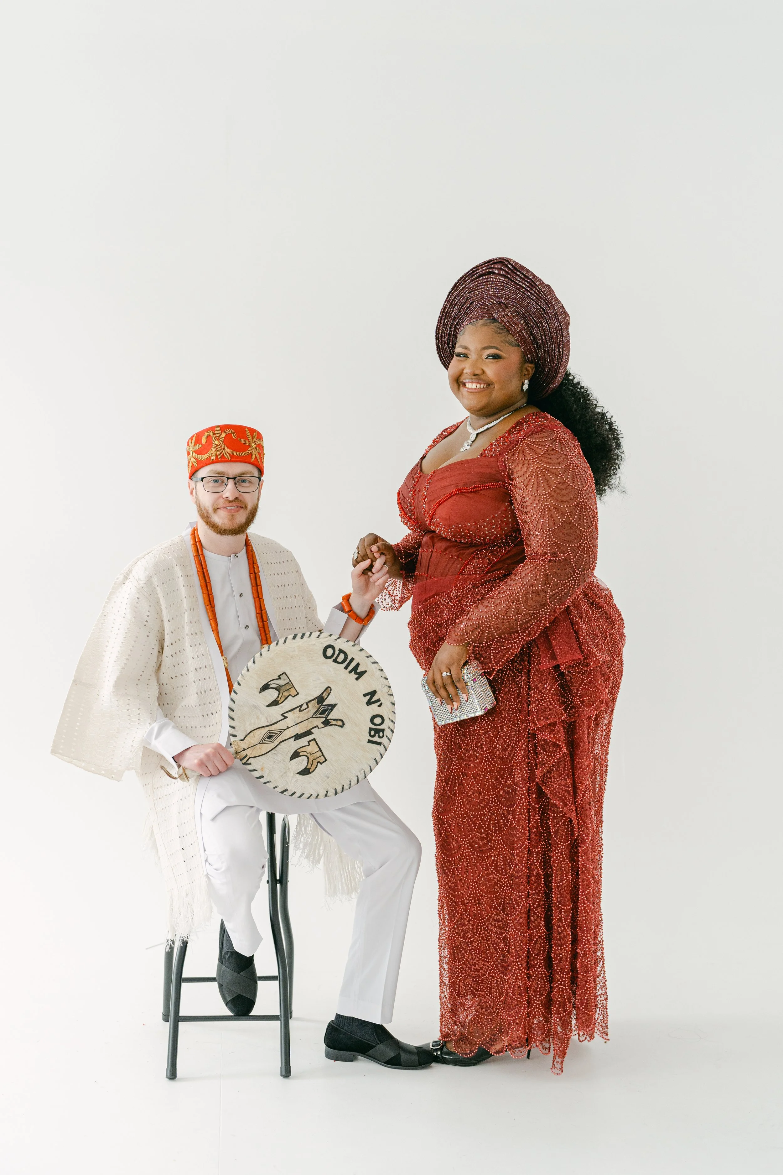 A couple pose together in elegant traditional attire during a cultural wedding portrait session, beautifully captured by Christy Photography. The rich textures, detailed beadwork and vibrant colours of their outfits stand out against the clean studio