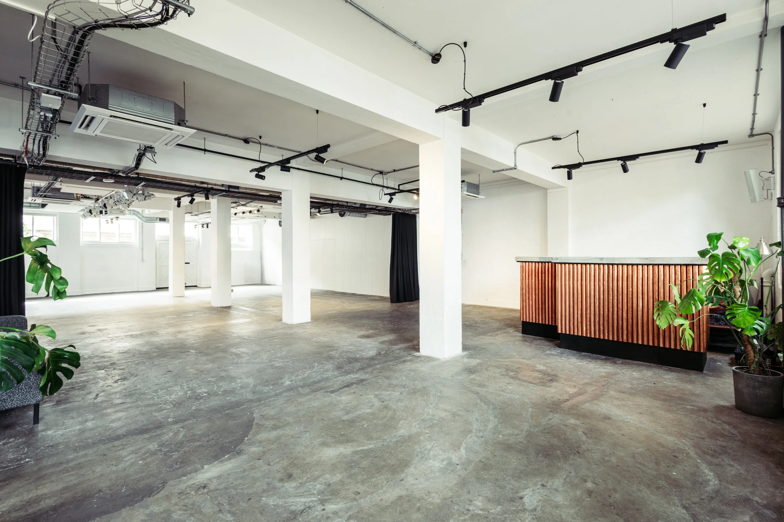 A bright, open-plan event space at Ministry 'I Do' Venues, featuring clean white columns, polished concrete floors and a contemporary wood-fronted bar - ideal for modern London weddings, receptions and creative celebrations.