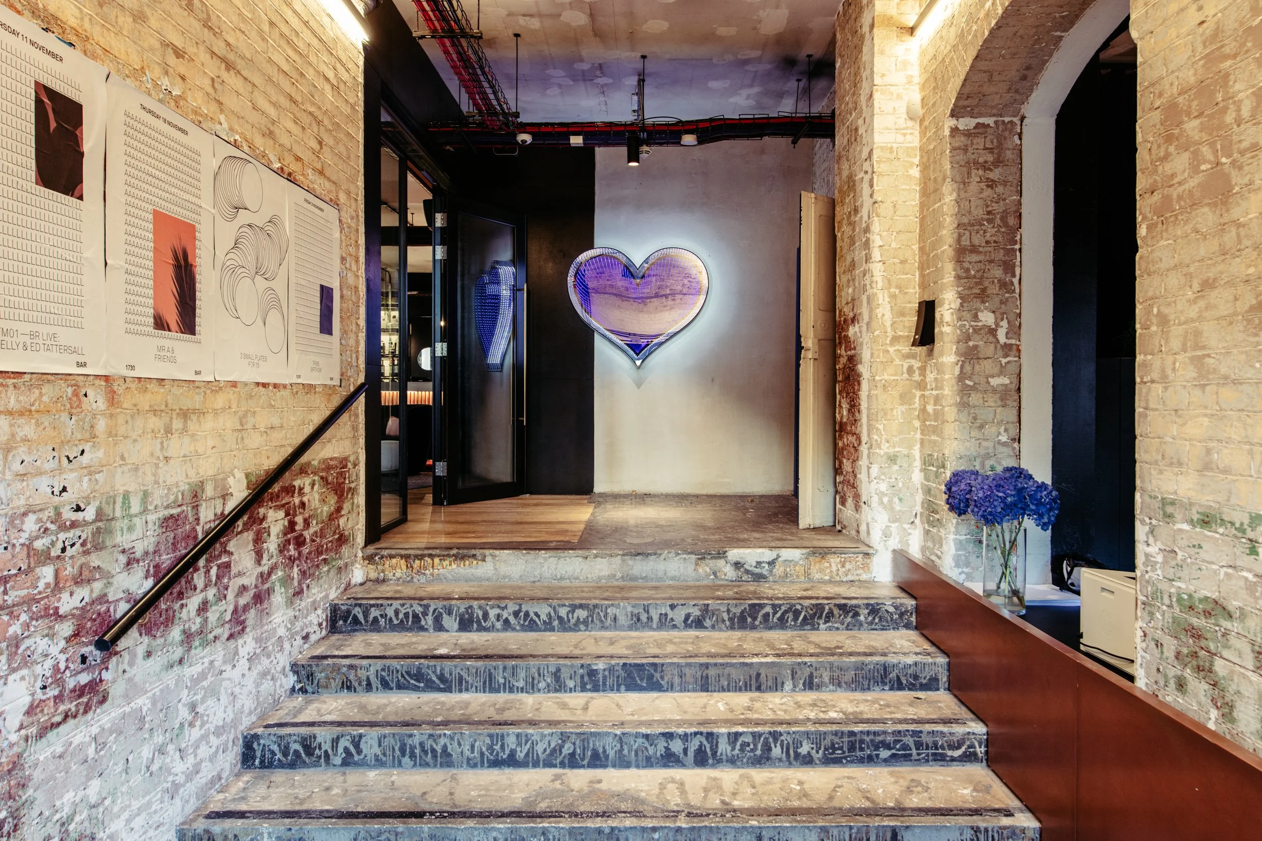 An atmospheric entrance at Ministry ‘I Do’, a stylish London wedding venue, featuring exposed brick walls, industrial details and a glowing heart installation - perfect for modern couples seeking a characterful, urban wedding setting.