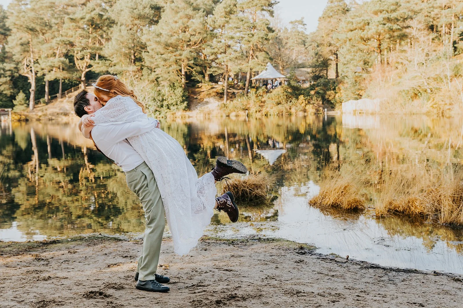 A happy couple in arms, celebrating in front of a beautiful lake at their outdoor wedding, styled by Wild Soul Weddings, eco wedding planners in the UK. Lotus Photography UK 