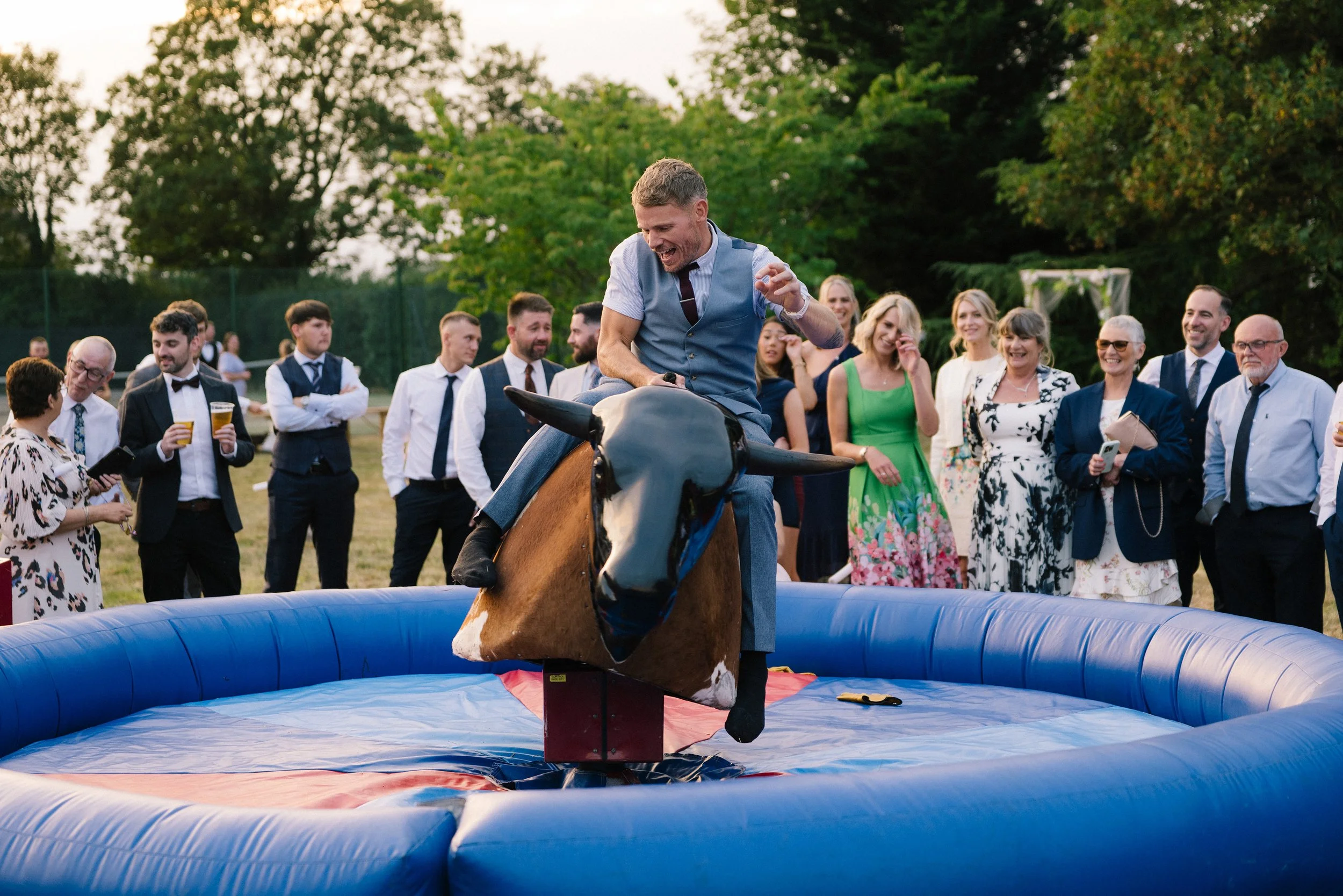 A fun high-energy moment brought to life by Big Sister Events, featuring a guest riding a bucking bronco as friends and family gather around cheering and laughing creating a lively, joy-filled atmosphere perfect for festival-style weddings, outdoor r