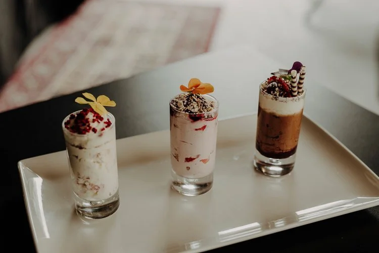 A trio of elegant mini desserts by Regis Banqueting, beautifully served in glass shot cups and garnished with edible flowers and chocolate curls. This refined wedding dessert selection showcases the caterer’s skill in creating visually stunning and d
