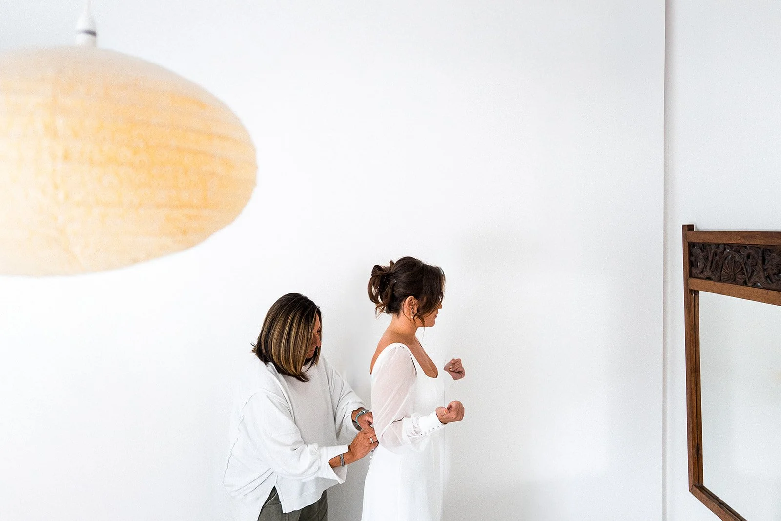 A bride being helped into her dress on the morning of her wedding.