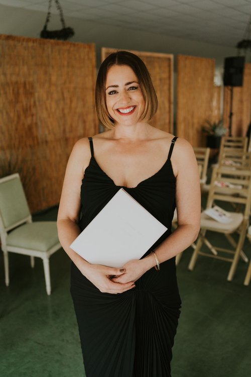 Portrait of wedding celebrant Vicky smiling and holding a folder in a ceremony space, representing Your Celebrant Vicky’s warm and personal approach to weddings.