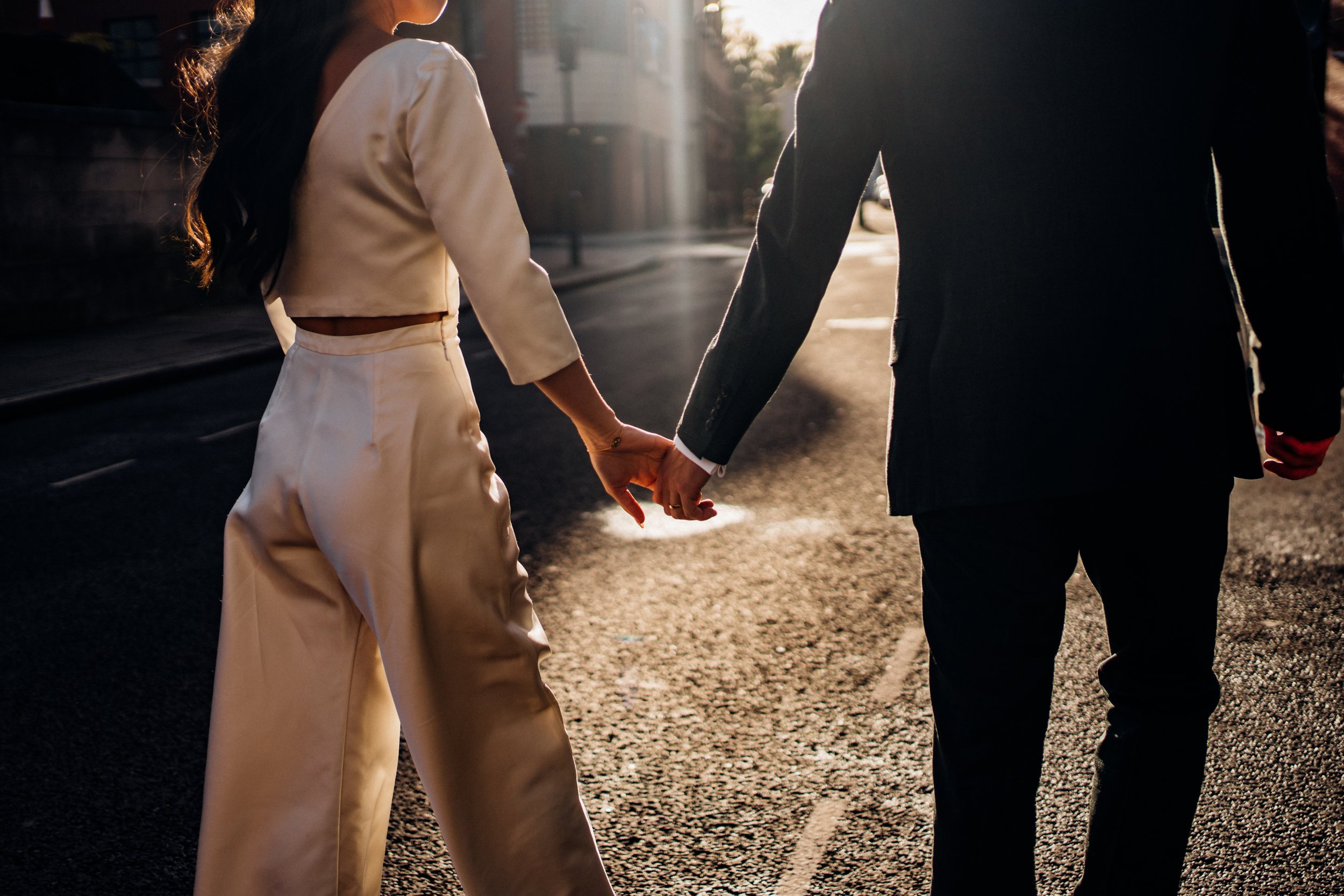 A nice cropped image of a modern wedding couple holding hands. The bride is wearing a stunning jumpsuit instead of a dress.