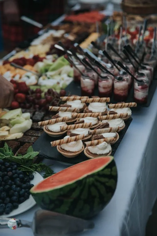 Beautiful wedding dessert table by Regis Banqueting, showcasing an array of mini tarts, fresh fruit, and layered dessert cups. Styled on an elegant white tablecloth with watermelon, blueberries, and pastries, this luxurious spread reflects the compan