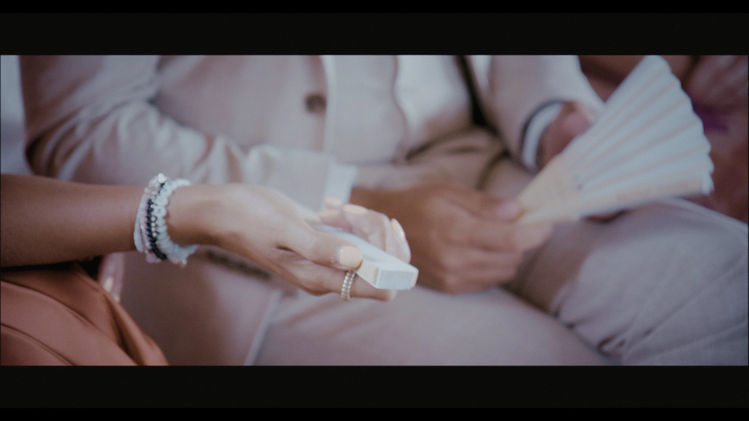 A soft, cinematic close-up from a Heart Shaped Video wedding film, capturing a tender, detailed moment as a guest holds a delicate bar of soap and a fan during the ceremony. The pastel tones, gentle focus, and natural light evoke warmth and intimacy,