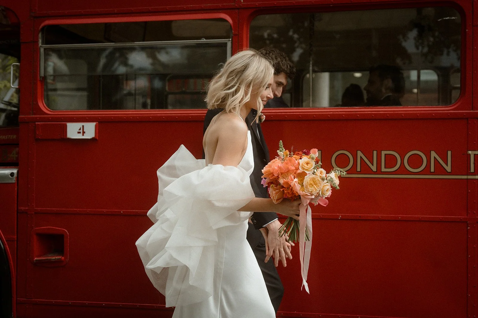 A couple moves through a series of cinematic wedding scenes that mix urban character with romantic intimacy as soft tulle sleeves catch the light, vivid bouquets glow against red London buses, and drifting clouds of colored smoke wrap them in a dream