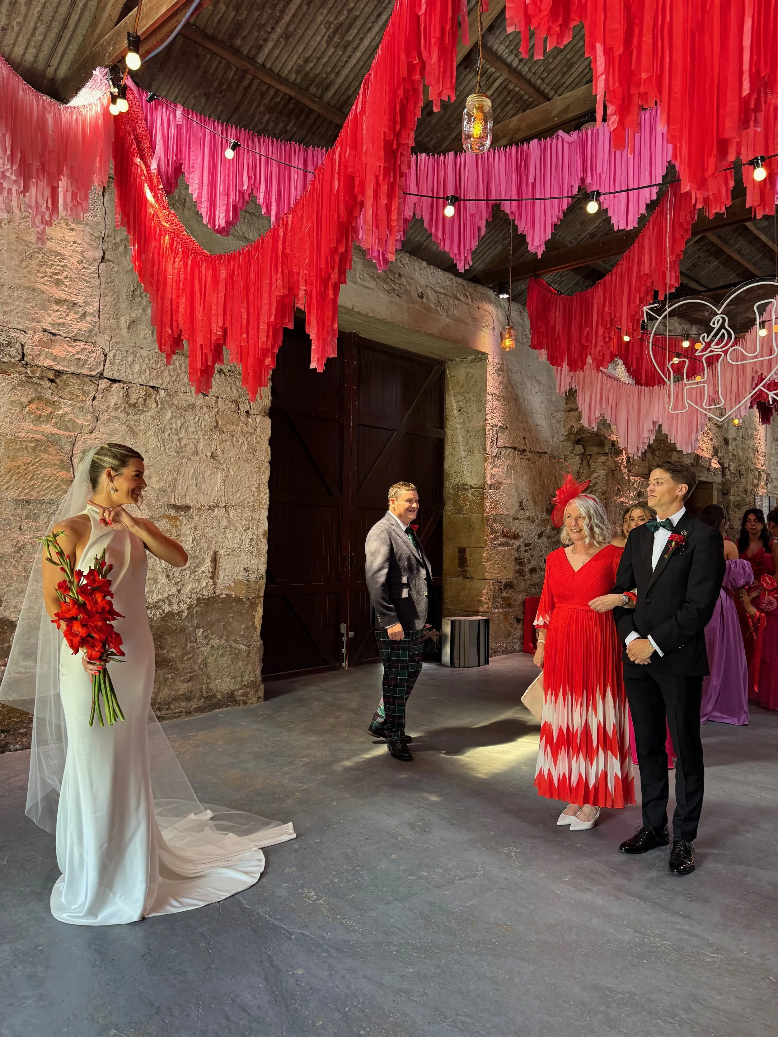 Streamadelica wedding décor installation with dramatic red and pink fringe ceiling, creating a bold, immersive ceremony space inside a rustic stone barn venue.