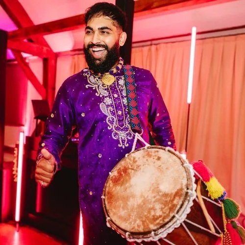Traditional dhol drummer performing at a wedding celebration, dressed in a vibrant embroidered outfit. The lively beats of the dhol bring energy, colour, and excitement to the dance floor, making it a perfect entertainment choice for Asian weddings, 