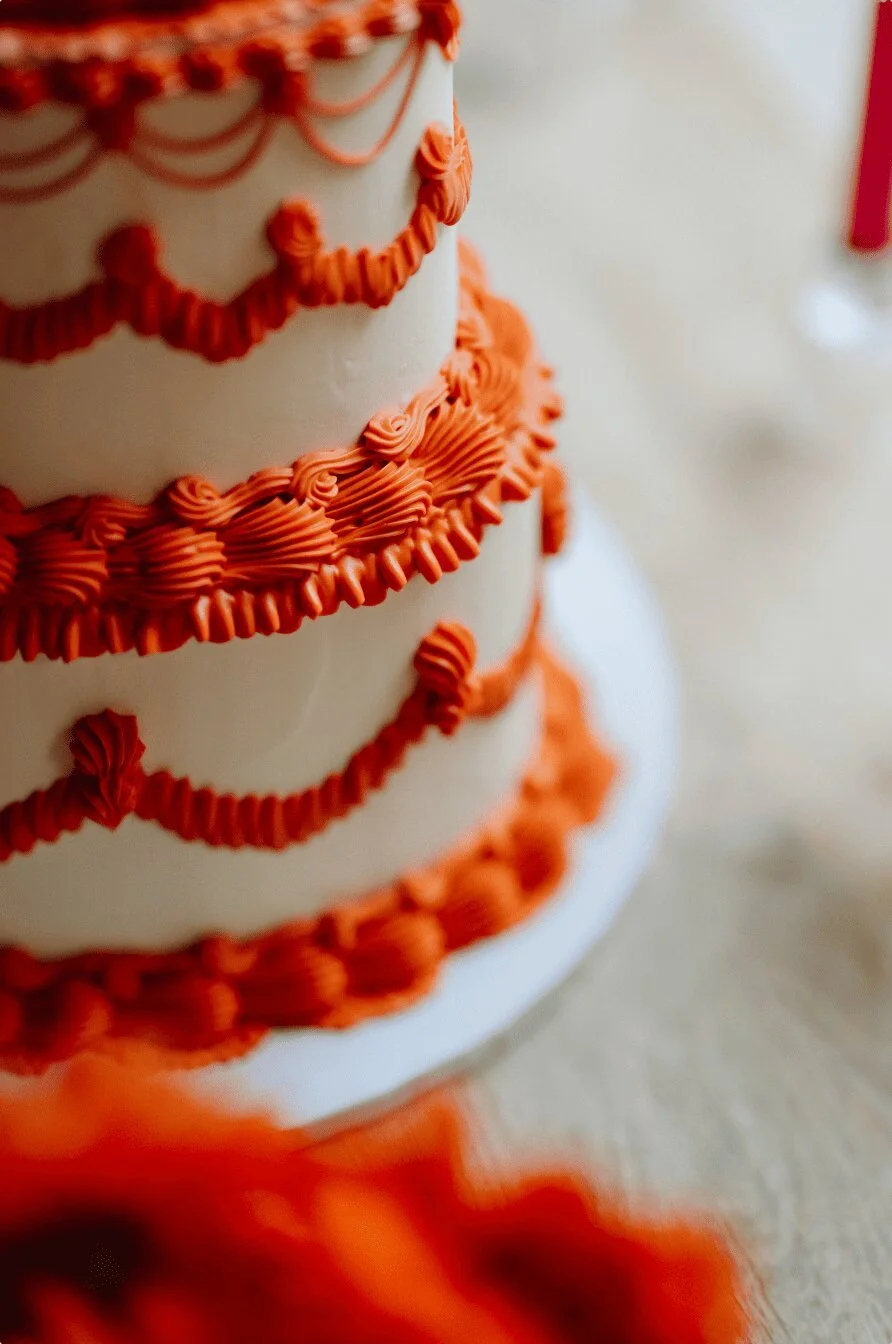 Close up of a retro-inspired wedding cake by The Cake Hun featuring tiered vintage piping, ivory buttercream and bold red detailing.