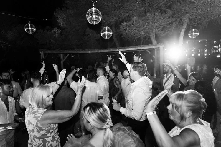 Guests dancing under disco balls and colourful lights at an outdoor wedding reception. The lively dance floor atmosphere captures family and friends celebrating together, perfect for couples wanting energetic wedding entertainment and unforgettable e