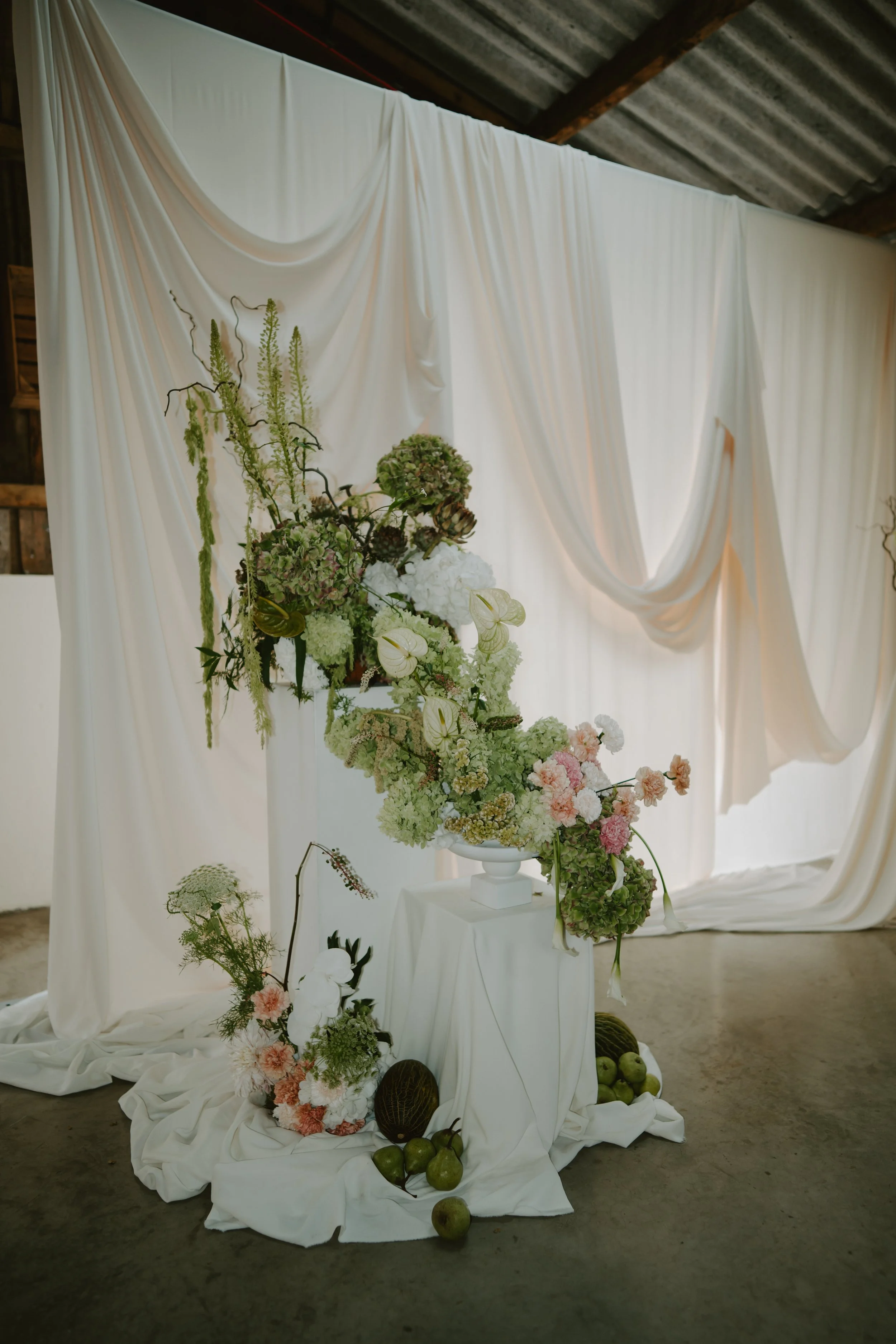 Orange Tree Weddings styling and décor showcasing a sculptural floral installation with soft draped fabric, seasonal blooms and organic textures, perfect for a modern, editorial wedding backdrop.