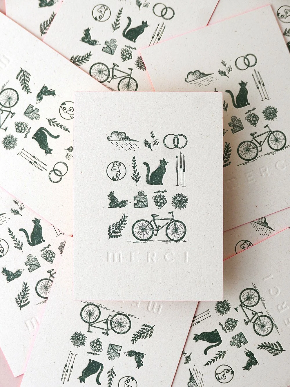 A playful wedding thank you card flatlay featuring illustrated green motifs including bicycles, cats, birds, foliage and wedding rings printed on textured recycled style card with a subtle embossed merci detail creating a charming artisanal aesthetic