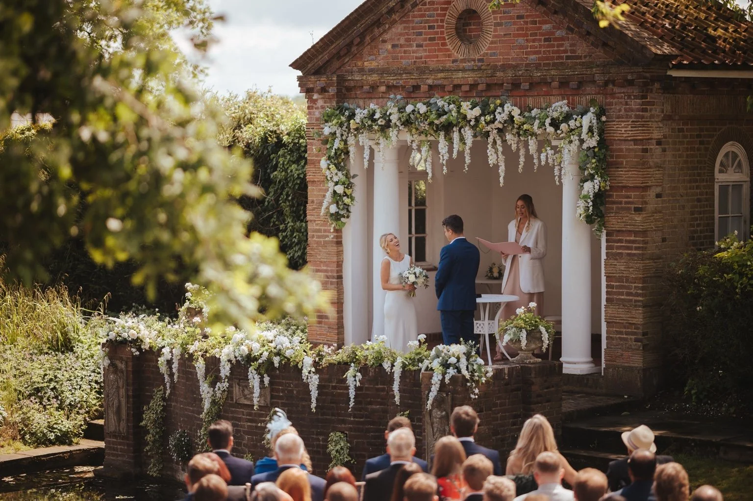 A beautiful outdoor wedding ceremony whith a celebrant who is wearing a white jacket. 