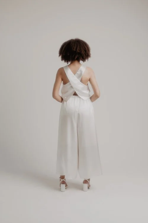 Sarah Barker bridal jumpsuit with wide-leg trousers and a statement cross-back bodice in soft ivory, photographed in a minimalist studio for modern wedding style inspiration.