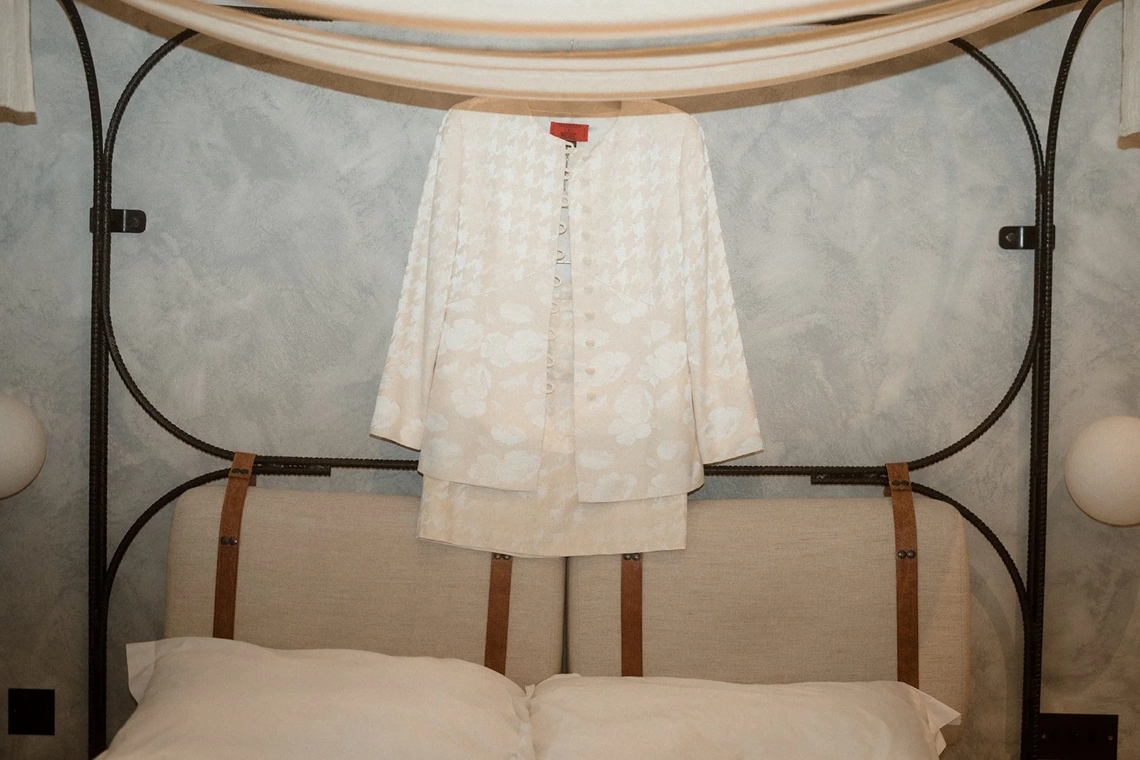 A vintage bridal suit hanging up on a modrn bed.