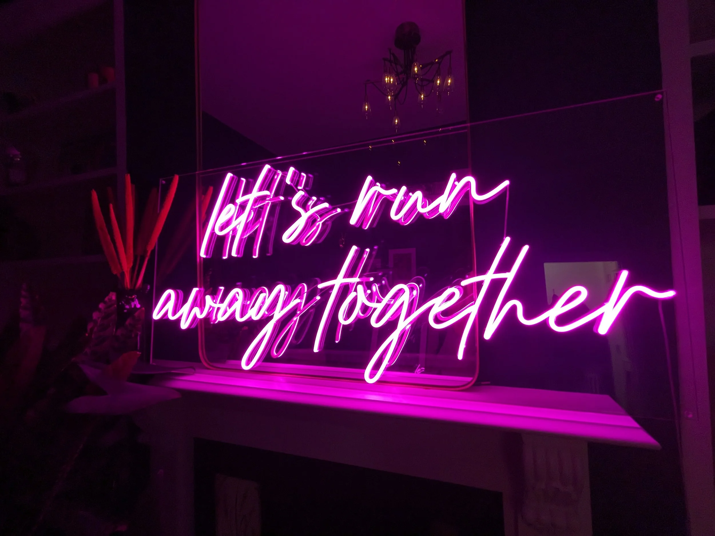 Romantic pink neon sign reading ‘let’s run away together’ glowing against a dark interior backdrop. The elegant handwritten-style LED light creates a dreamy, modern ambiance - perfect for weddings, proposals, or stylish home décor. Ideal inspiration 