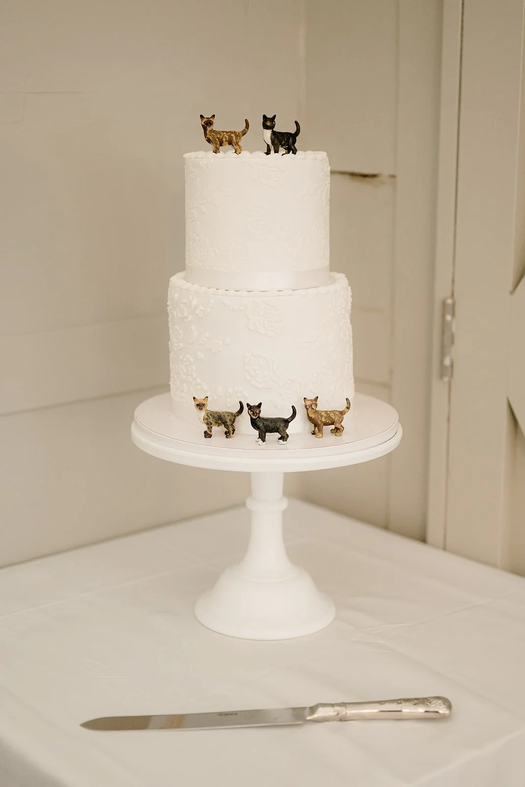 A 2 tier wedding cake with 5 cat ornaments on it. It's very simple and cute.