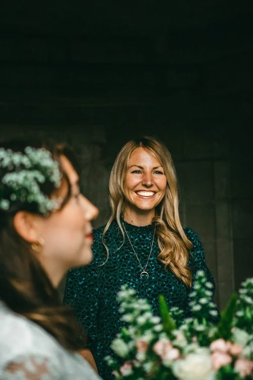 Roxy beside a couple during their intimate ceremony, surrounded by soft floral details and natural light. Dressed in a stylish green dress, the celebrant brings warmth and personality to the moment, reflecting the relaxed and modern approach of UK we