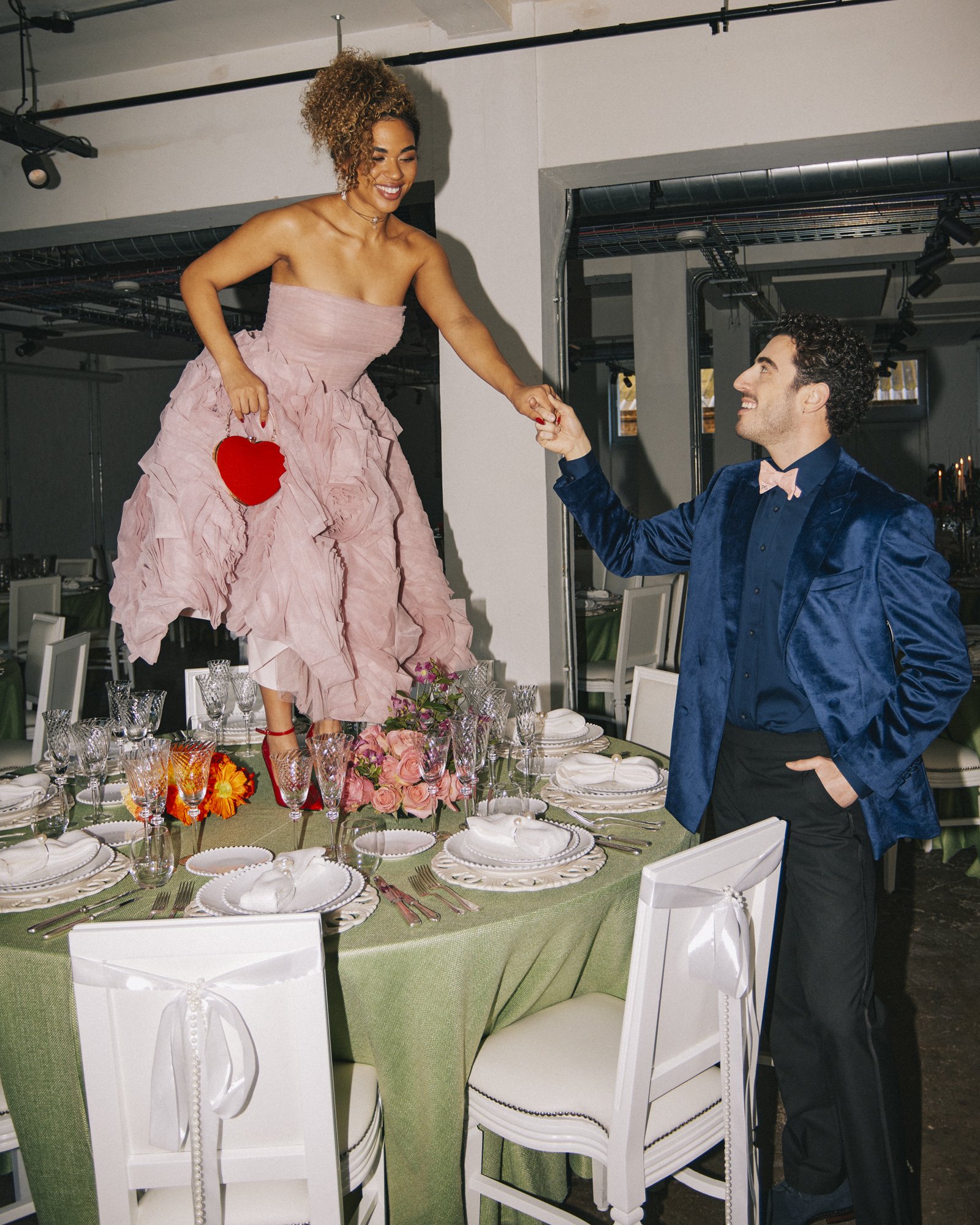 A playful, fashion-forward wedding moment at Ministry Venues, capturing a stylish couple interacting around an immaculately styled reception table, with elegant place settings, crystal glassware and floral centrepieces set within the venue’s modern i