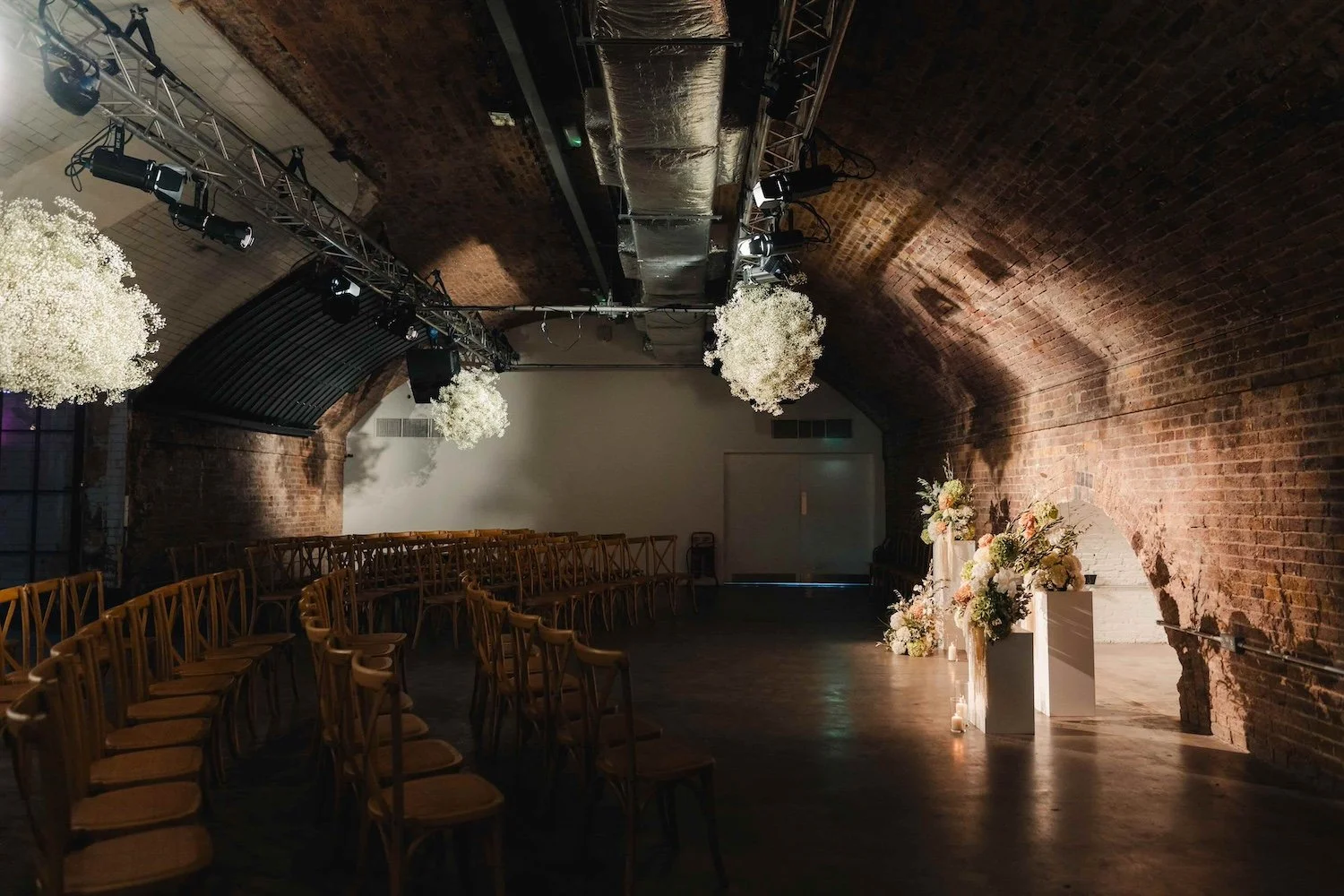 An atmospheric wedding set up at Kachette in East London. There are flower coulds suspended from the arched ceiling. The flowers are by Kitty Willow and the photo is by The Chamberlains.