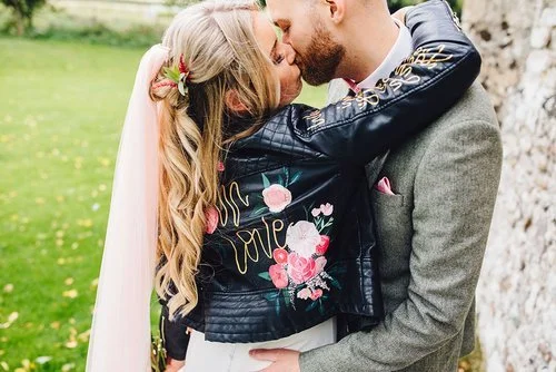 Romantic wedding moment featuring a hand-painted leather jacket by Bee Davies Illustration. The bespoke “Mrs” design with pink floral artwork adds a stylish, personalised touch - perfect for brides looking for custom wedding fashion and creative keep