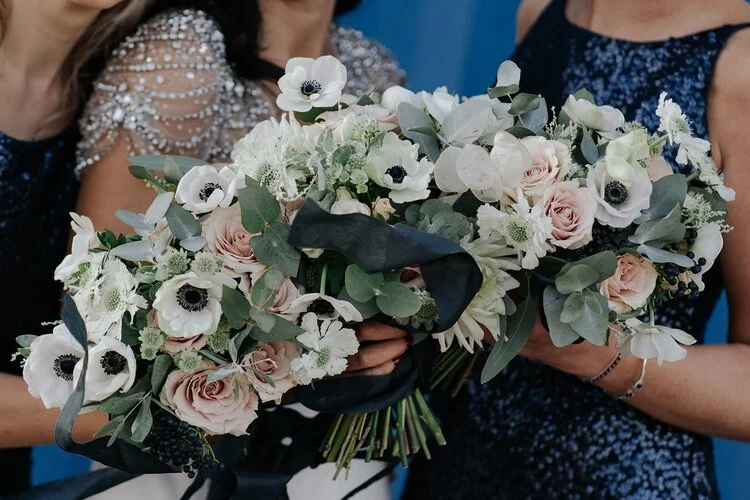 Chic bridesmaid bouquets by Catherine Short Florals featuring soft blush roses, white anemones, astrantia and eucalyptus tied with dark silk ribbons. Paired with elegant navy and beaded dresses, these refined modern arrangements highlight Catherine S