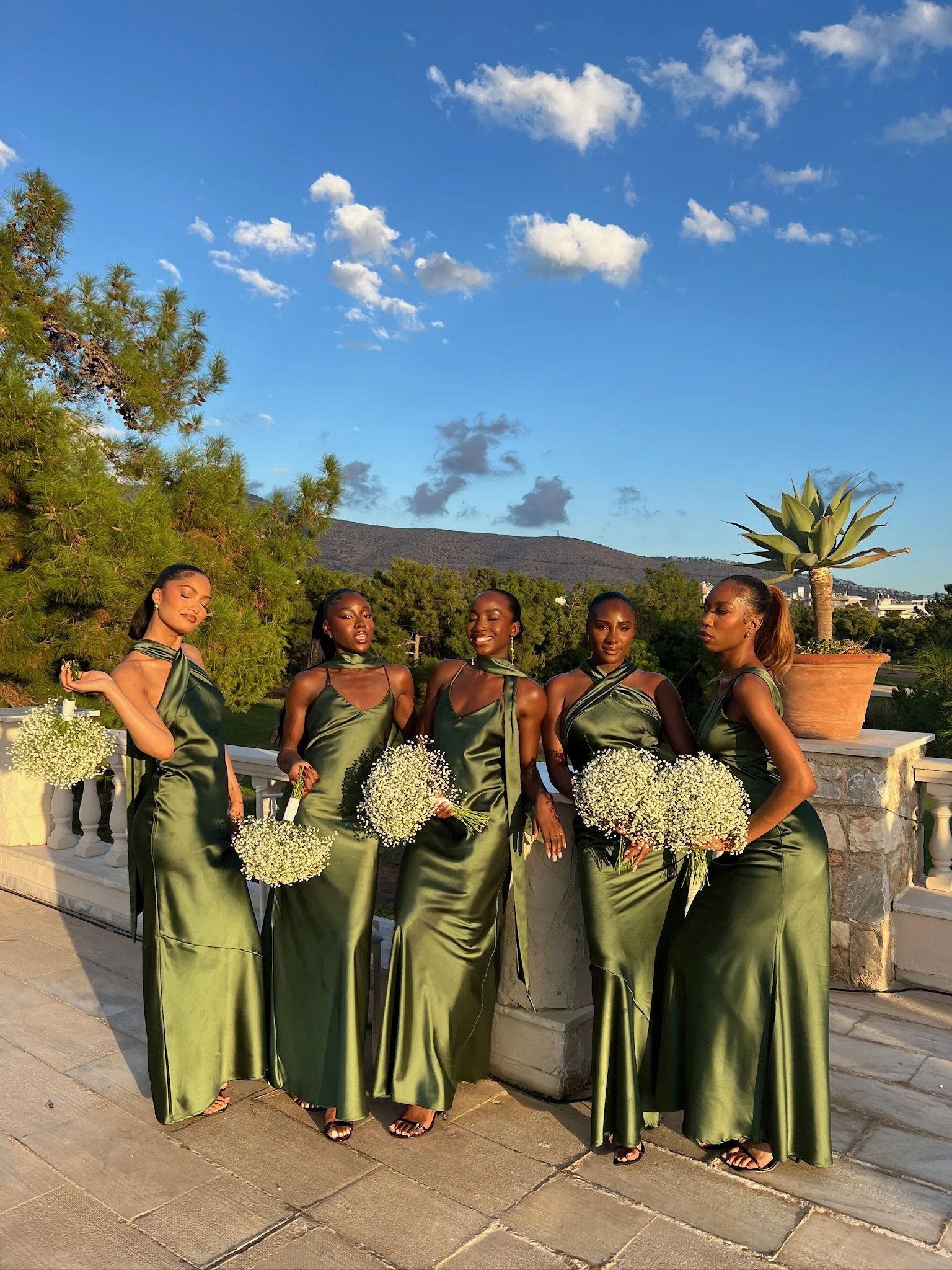 An outdoor shot of a bride and her bridesmaids. They are all wearing different style green dresses from Rewritten London.