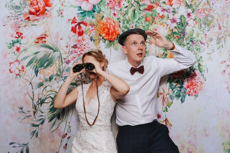 A fun wedding photo captured in the Flash Fox Photo Booth, featuring a bride and groom striking playful poses against a bright floral backdrop. This colourful and creative setup adds personality and joy to any celebration, giving guests the chance to