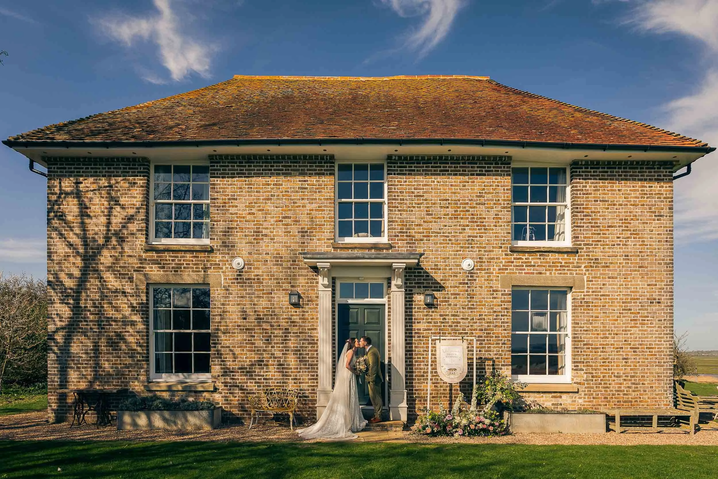 A bride and groom kissing outside Elmley Nature Reserve on their summer wedding day.