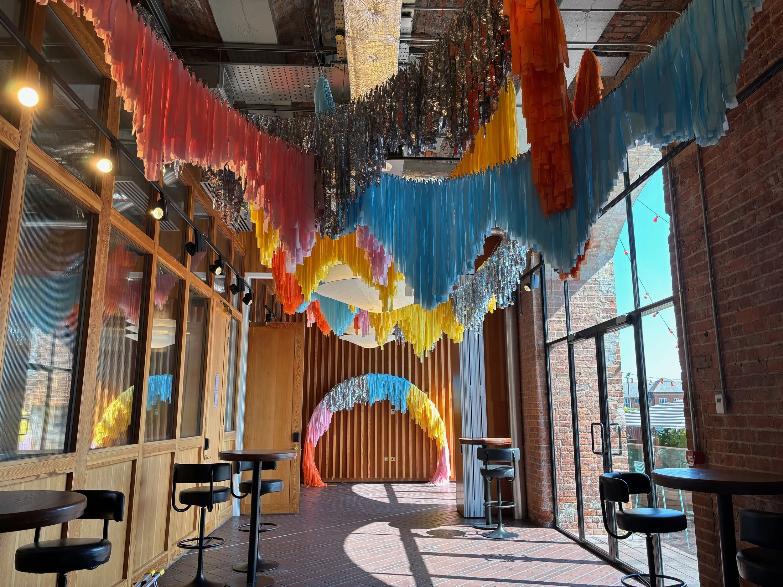 Streamadelica immersive wedding installation with cascading multicolour fringe ceiling and matching rainbow arch, transforming an industrial venue into a vibrant, modern wedding and party space.