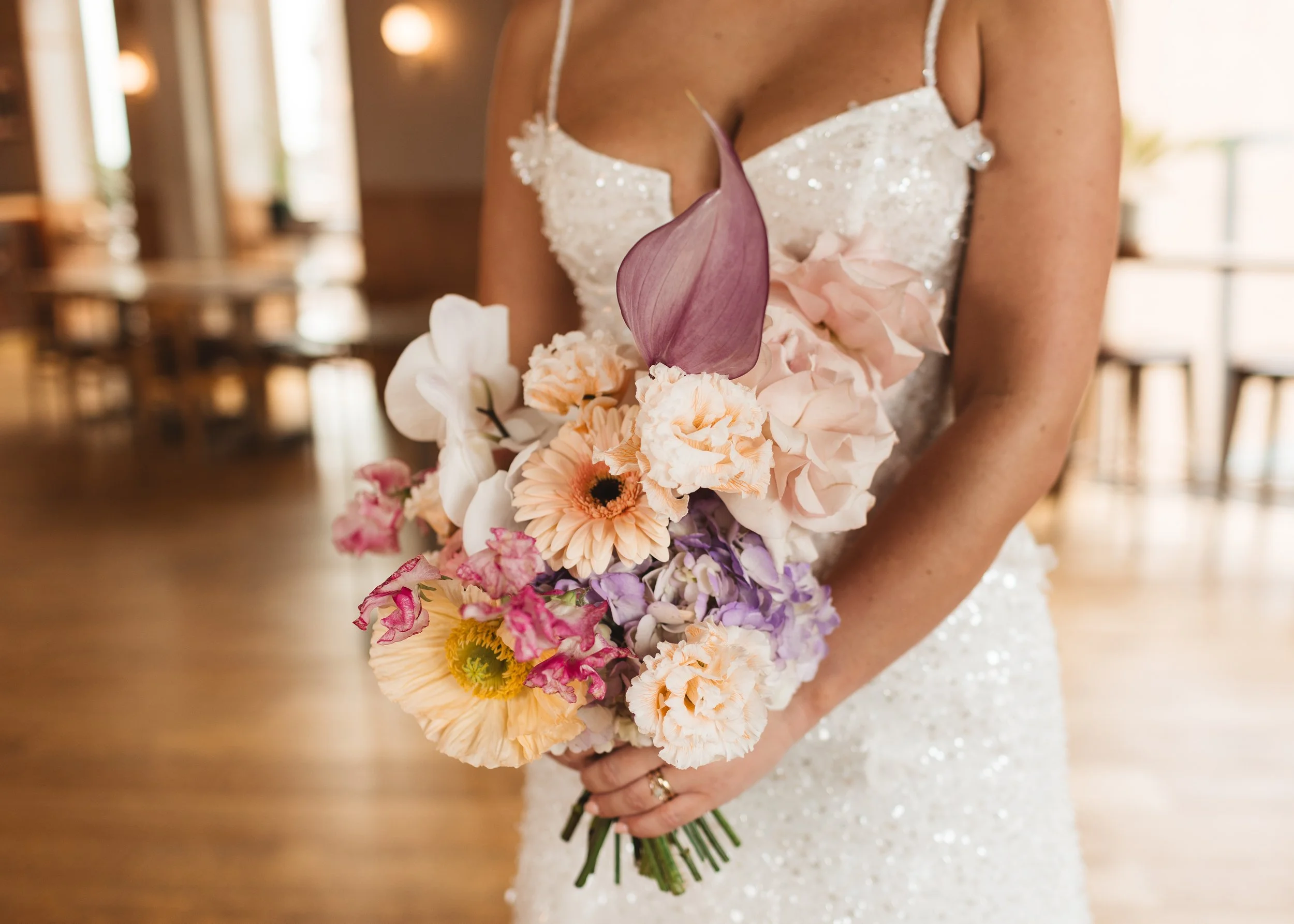 Modern bridal bouquet by Sweet Pea Sorbet Floristry featuring pastel-toned blooms including blush roses, lilac calla lily, peach gerbera daisies, white orchids, and soft purple delphiniums. Captured by Hollie Carlin Photography, held by a bride in a 