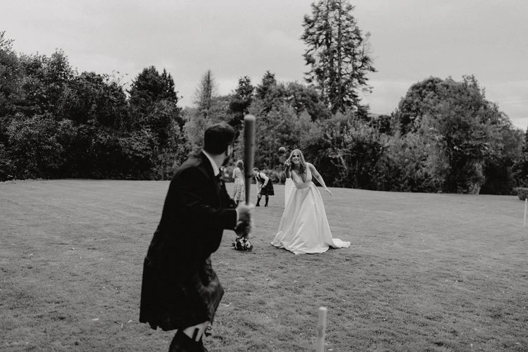 A fun, candid moment as the newlyweds play an energetic game on the lawn, captured in timeless black and white by F.D Young Photography. The bride laughs mid-throw while the groom, dressed in traditional Scottish attire, prepares to swing, creating a