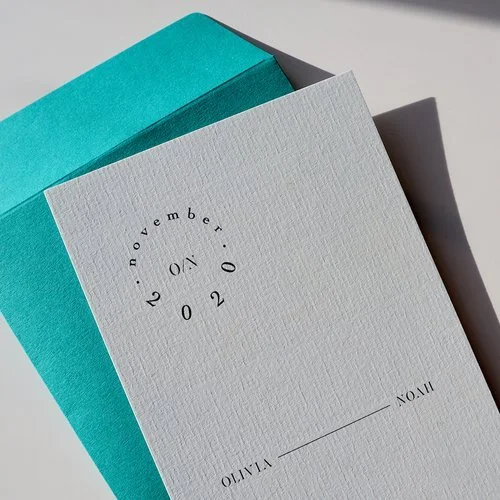 Elegant minimalist “Save the Date” card by Pelirocco Design. Featuring clean black typography on textured white card with a bold turquoise envelope, this refined modern design is perfect for couples who love simple, contemporary wedding stationery cr
