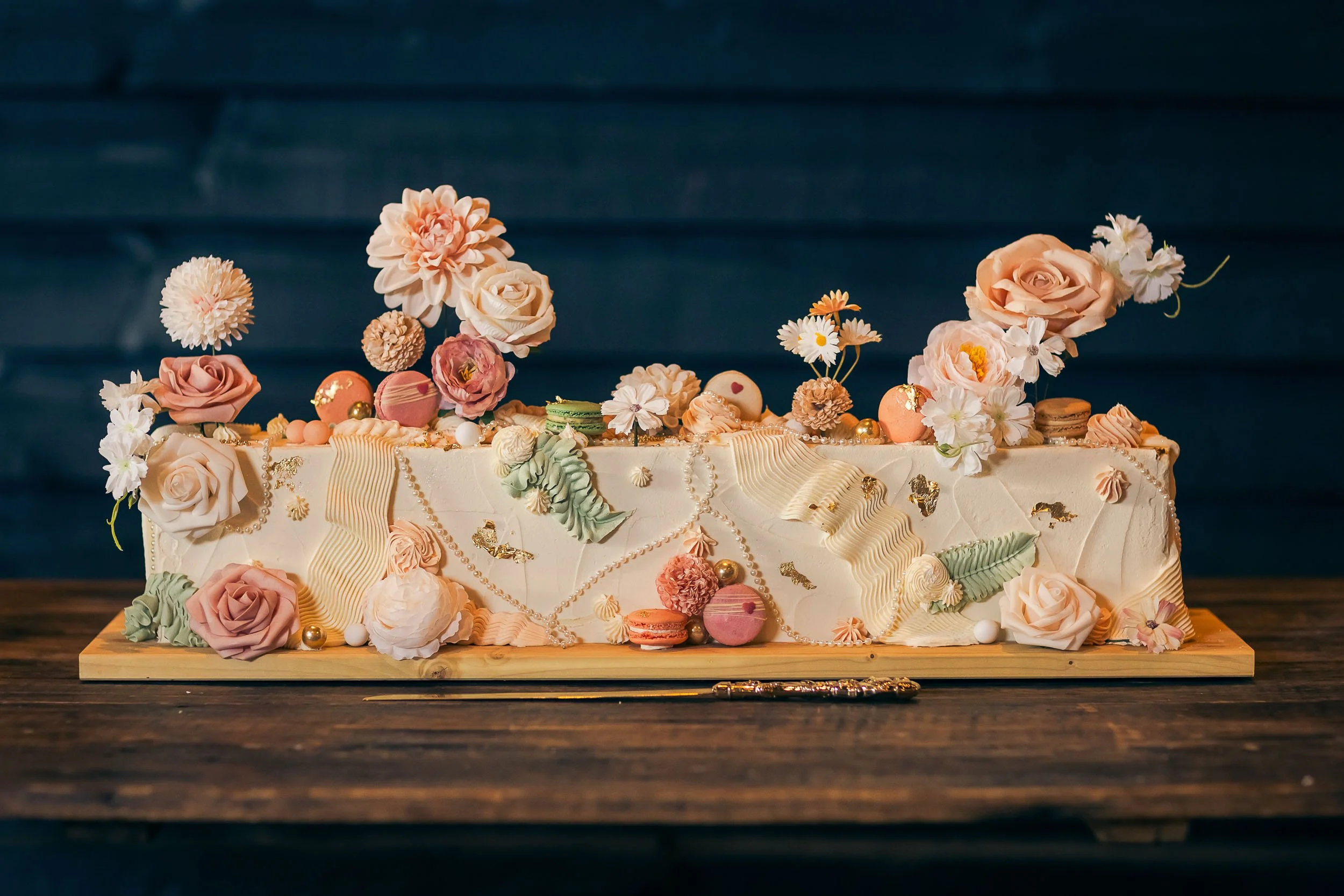 An ornate sheet cake with fresh flowers and macarons.