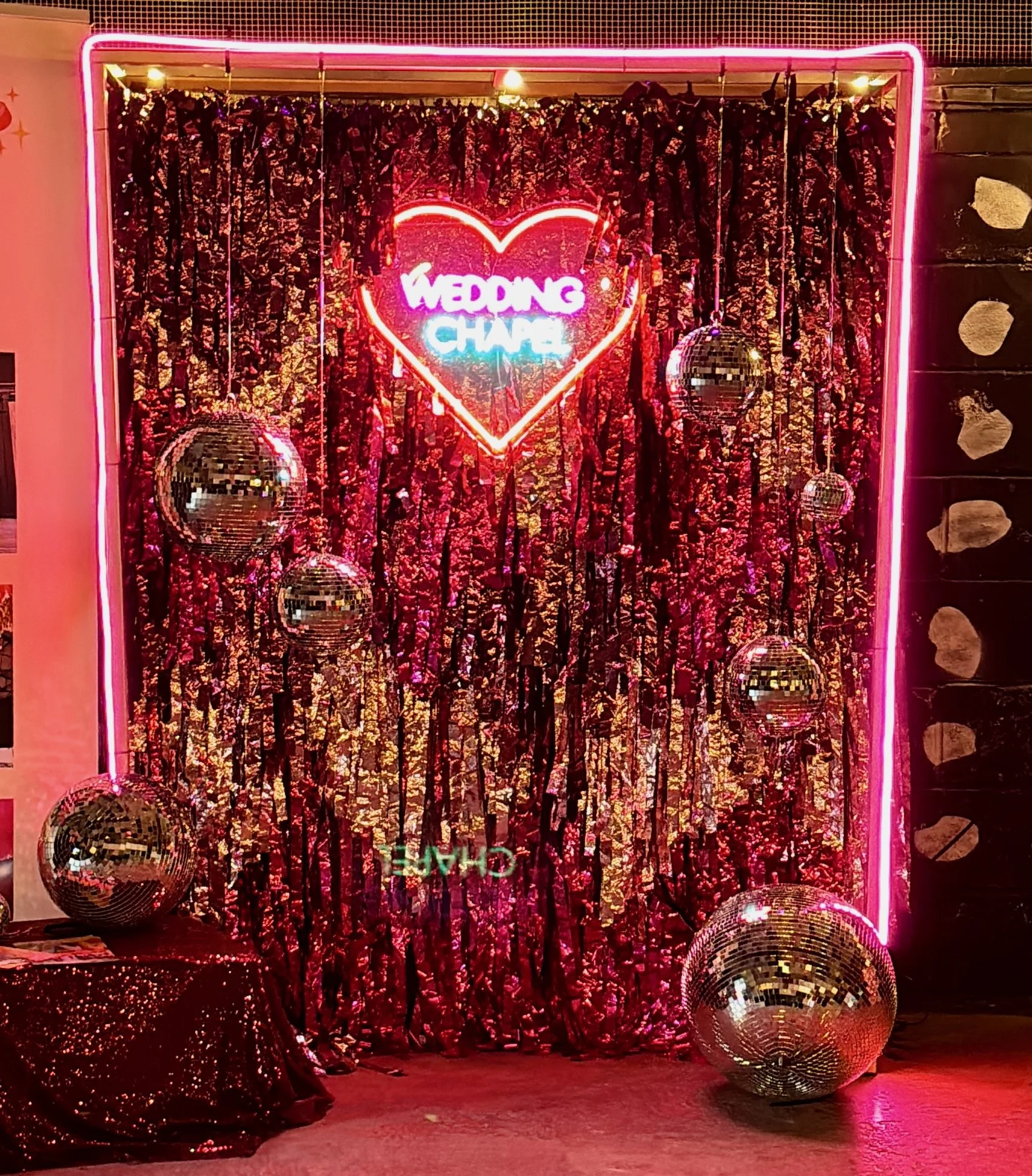 Streamadelica wedding backdrop featuring neon “Wedding Chapel” sign, pink sequin curtain and disco balls, creating a playful, retro-inspired wedding photo moment full of colour and sparkle.