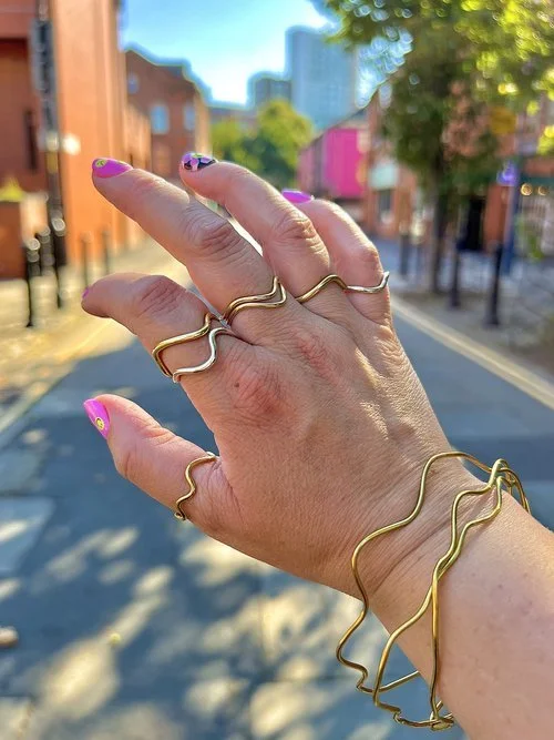 Modern wavy gold and silver rings and bangles by Stacey Hill Jewellery, styled in a vibrant street setting. Handcrafted in the UK, these sculptural designs are perfect for brides seeking bold, contemporary wedding jewellery.
