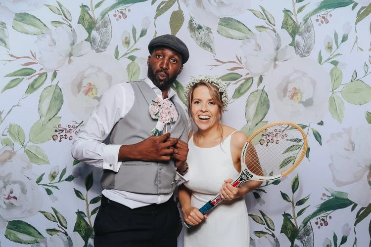 A joyful wedding photo from the Flash Fox Photo Booth, showing a couple striking playful poses with fun props against a floral backdrop. Their laughter and creativity capture the relaxed, lighthearted energy of modern UK weddings. This photo booth ex