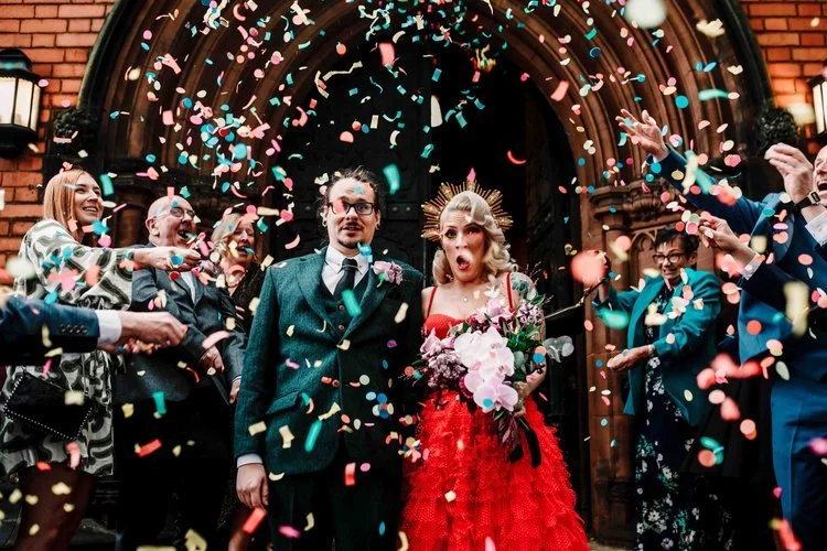 A lively and joy filled wedding moment captured by Amy Faith Photography, showing the couple swept up in the energy of a street brass band parade. The bride beams as musicians surround her with trumpets, saxophones and a sousaphone, creating a vibran