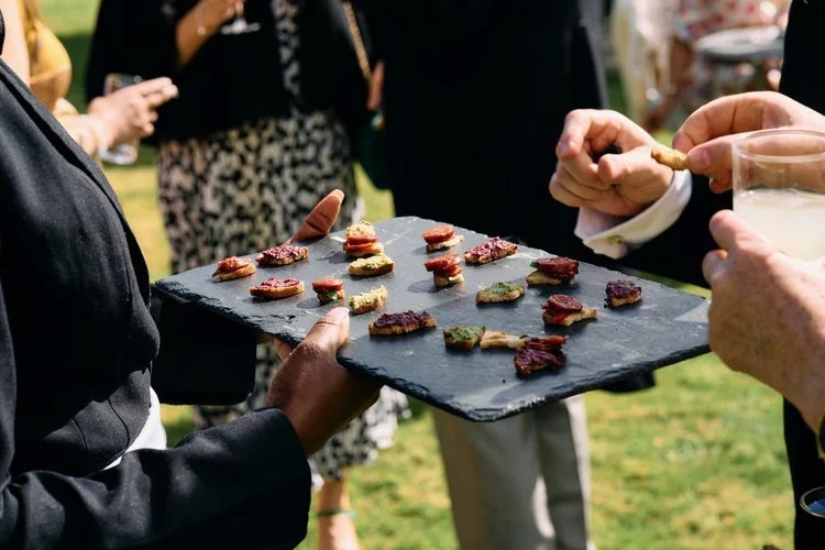 A server presents a stylish slate tray of colourful canapés to wedding guests during a garden reception. The beautifully plated bites reflect Tasting Plates Wedding Caterers’ focus on fresh, seasonal ingredients and elegant presentation, perfect for 