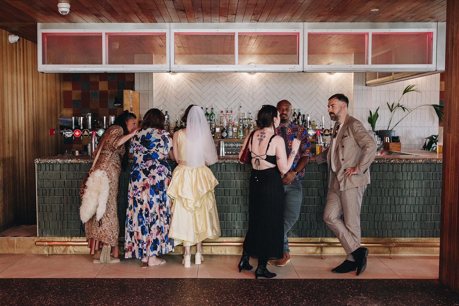Wedding guests gather at the bar inside Pier Court Wedding Venue in Brighton, capturing a relaxed, social atmosphere in a modern seaside wedding setting.
